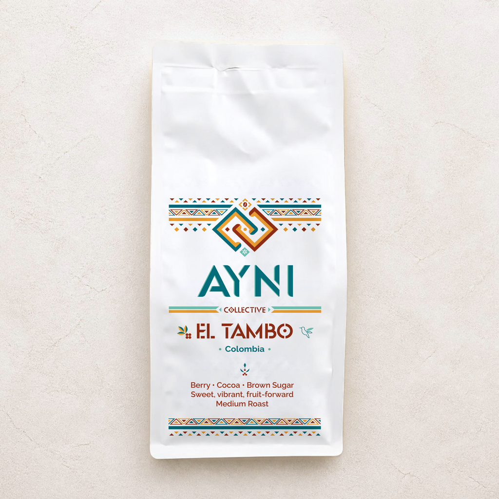 A white bag of Ayni Collective El Tambo Colombia coffee, featuring colorful geometric patterns and product details, set against a textured light beige background.